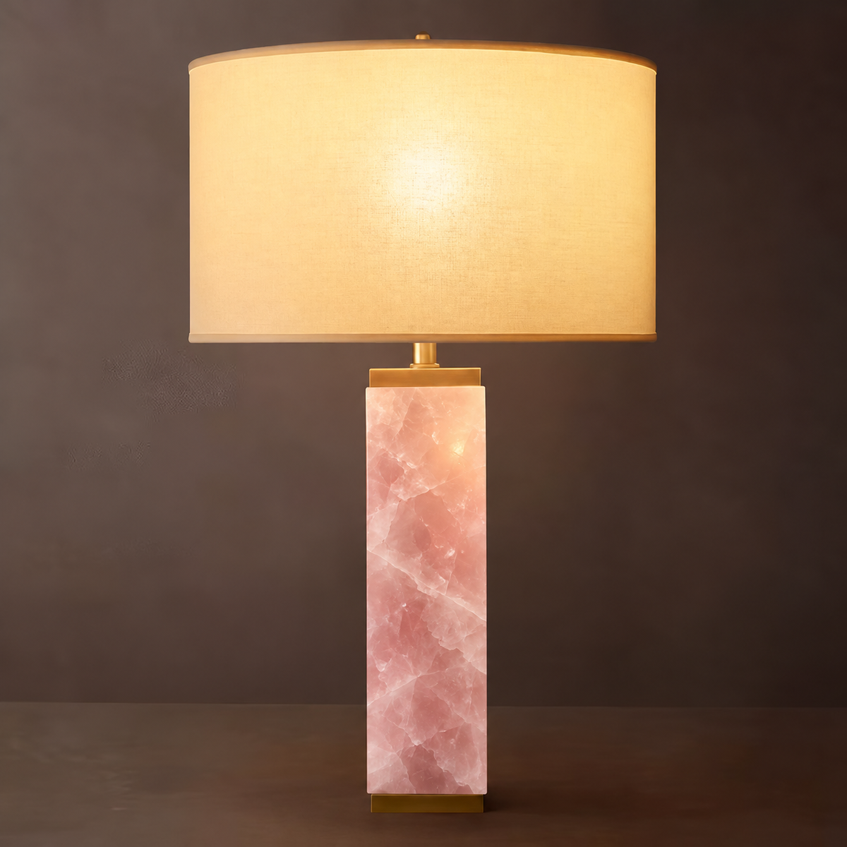 Serra rose quartz column table lamp lit, with brass cap and ivory linen drum shade