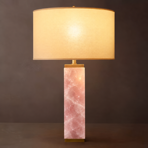 Serra rose quartz column table lamp lit, with brass cap and ivory linen drum shade