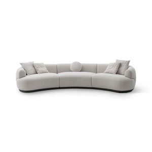 Maison Debrah Lunève curved three-section sofa in warm oatmeal fabric on a dark grey plinth