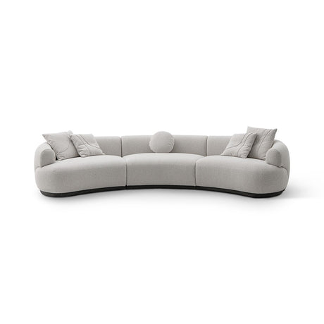 Maison Debrah Lunève curved three-section sofa in warm oatmeal fabric on a dark grey plinth