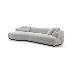 Maison Debrah Lunève curved three-section sofa in warm oatmeal fabric on a dark grey plinth — view 3